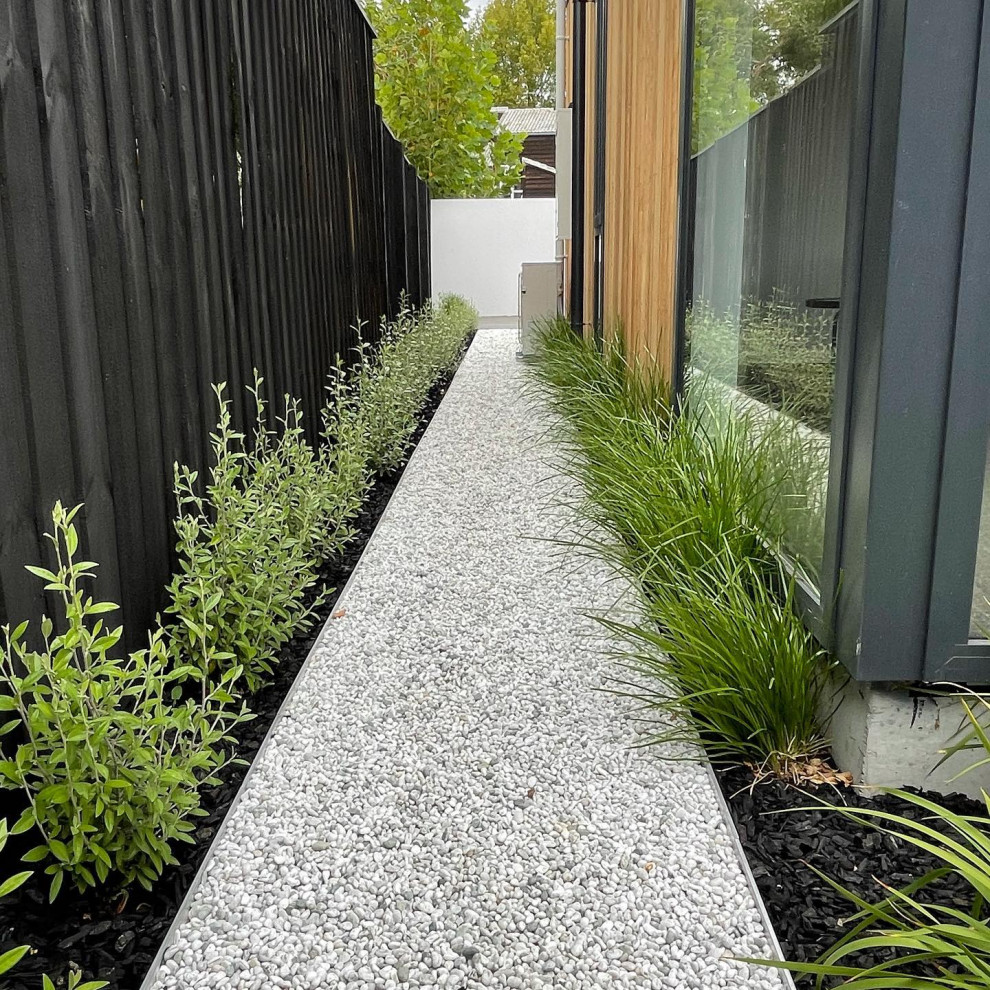 Small modern side yard shaded xeriscape in Christchurch with with path, river rock and a wood fence for winter.