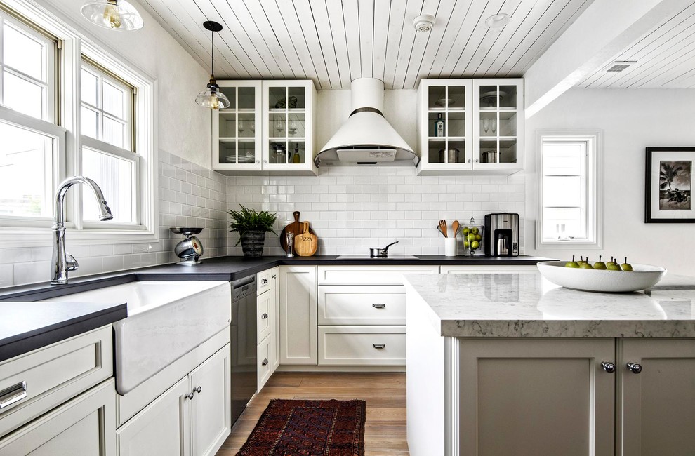 Design ideas for a transitional l-shaped open plan kitchen in Other with a farmhouse sink, white cabinets, white splashback, glass tile splashback, white appliances, light hardwood floors, with island and brown floor.