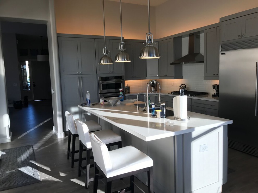 Example of a mid-sized transitional l-shaped porcelain tile and gray floor open concept kitchen design in Phoenix with an undermount sink, shaker cabinets, gray cabinets, quartzite countertops, white backsplash, glass tile backsplash, stainless steel appliances and an island