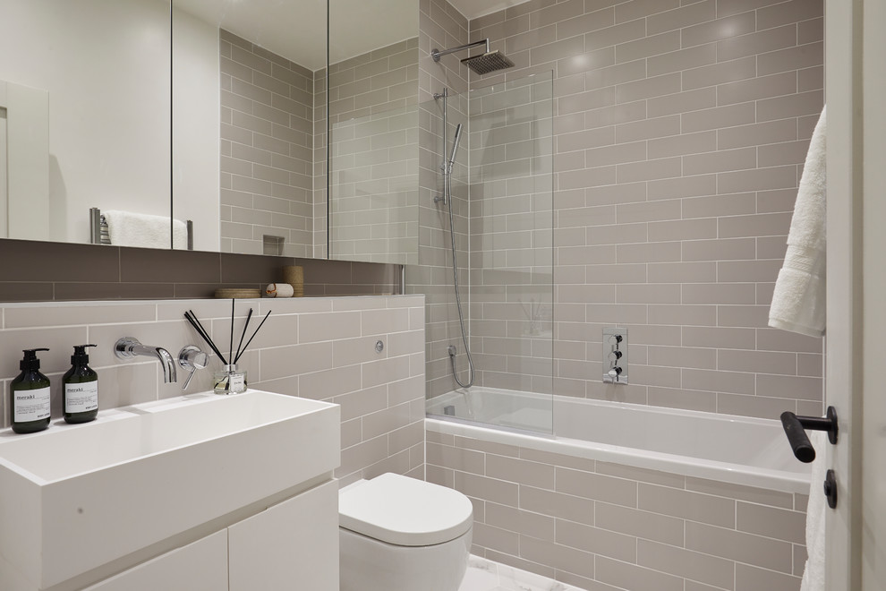 This is an example of a contemporary bathroom in London with flat-panel cabinets, white cabinets, an alcove tub, a shower/bathtub combo, gray tile, subway tile, white floor, an open shower and a console sink.