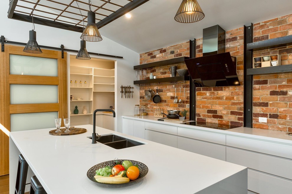 Photo of a large l-shaped eat-in kitchen in Other with an undermount sink, black cabinets, quartz benchtops, red splashback, brick splashback, stainless steel appliances, with island, brown floor and white benchtop.