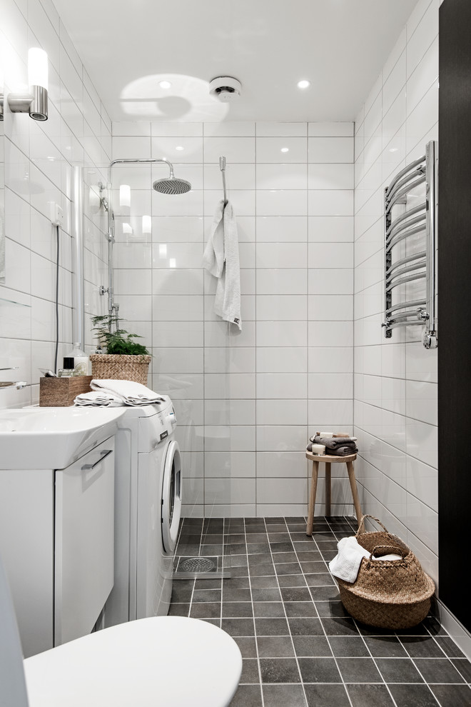 Mid-sized scandinavian bathroom in Stockholm with flat-panel cabinets, white cabinets, white tile, black floor, a one-piece toilet, white walls, a vessel sink and a laundry.