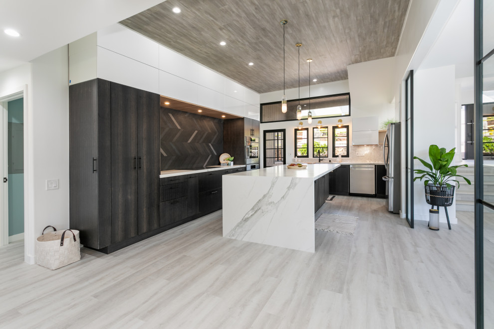 This is an example of a large modern u-shaped eat-in kitchen in Hawaii with a farmhouse sink, flat-panel cabinets, quartz benchtops, ceramic splashback, stainless steel appliances, vinyl floors, with island, grey floor, white benchtop and wood.