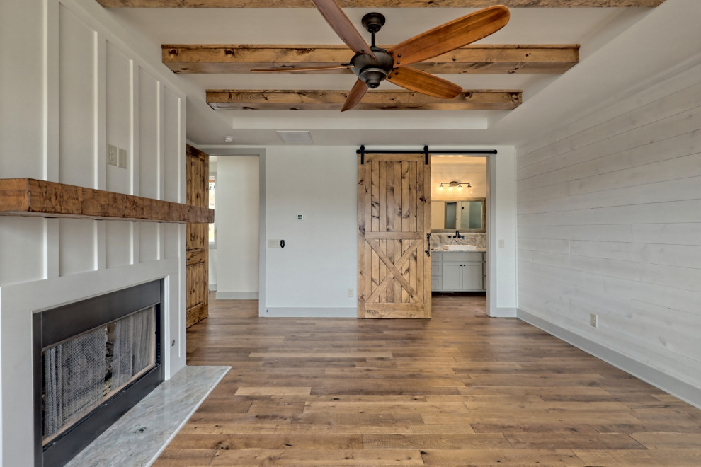 Photo of a large country master bedroom in Atlanta with white walls, medium hardwood floors, a standard fireplace, a wood fireplace surround, brown floor, exposed beam and planked wall panelling.