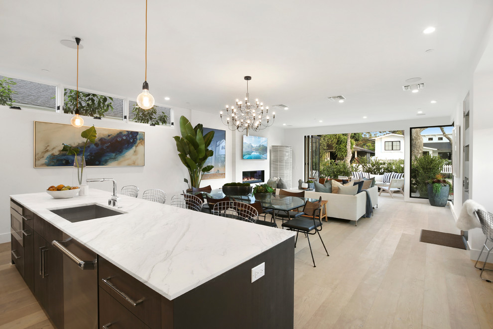 This is an example of a contemporary eat-in kitchen in Orange County with flat-panel cabinets, dark wood cabinets, marble benchtops, beige splashback, brick splashback, stainless steel appliances, light hardwood floors, with island, beige floor and white benchtop.