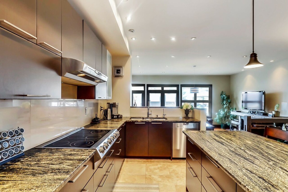 Example of a large transitional l-shaped travertine floor open concept kitchen design in Calgary with a double-bowl sink, flat-panel cabinets, dark wood cabinets, granite countertops, beige backsplash, stainless steel appliances and an island