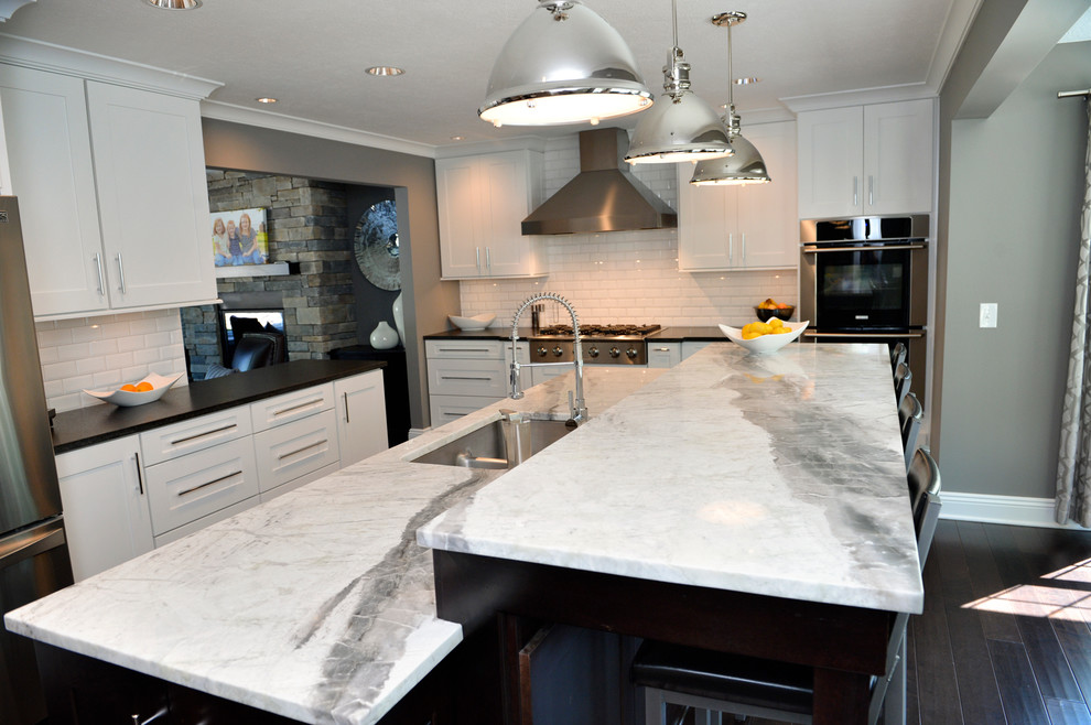Kitchen - transitional dark wood floor kitchen idea in Cleveland with a drop-in sink, recessed-panel cabinets, white backsplash, ceramic backsplash, stainless steel appliances and an island