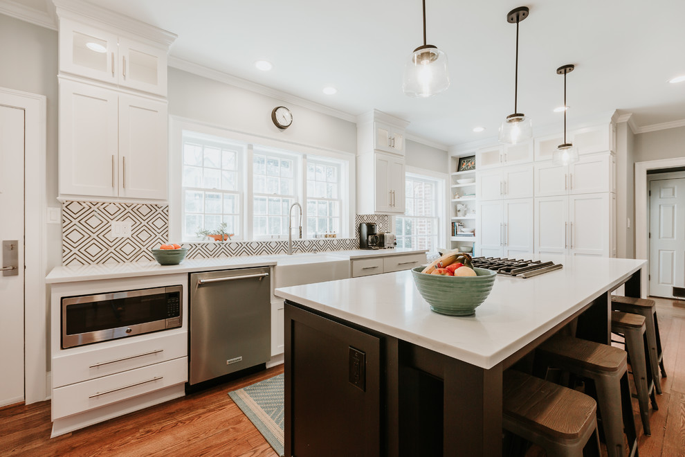 Inspiration for a transitional medium tone wood floor and brown floor kitchen remodel with a farmhouse sink, shaker cabinets, white cabinets, white backsplash, paneled appliances, an island and white countertops