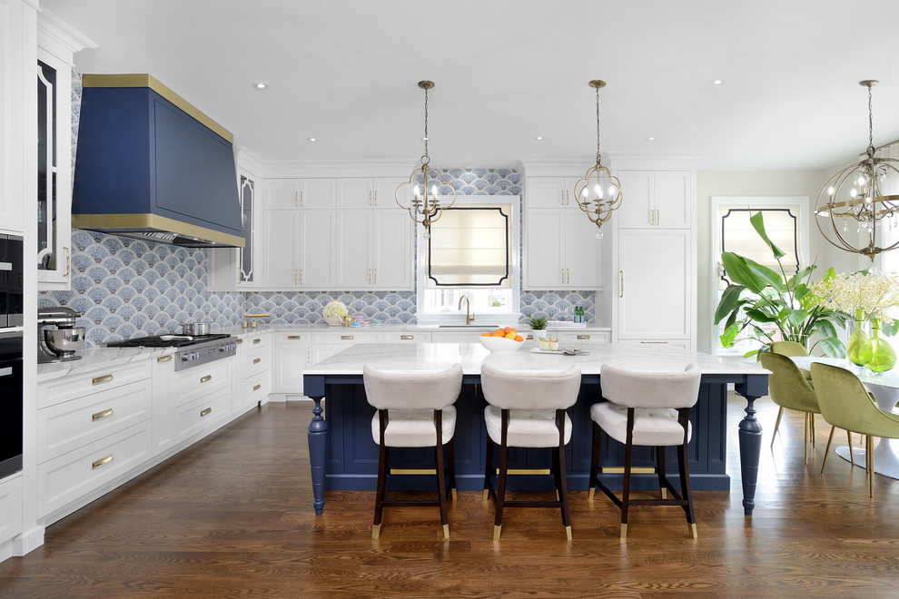 This is an example of a large traditional l-shaped eat-in kitchen in Toronto with an undermount sink, recessed-panel cabinets, white cabinets, quartz benchtops, blue splashback, mosaic tile splashback, stainless steel appliances, medium hardwood floors, with island, brown floor and white benchtop.