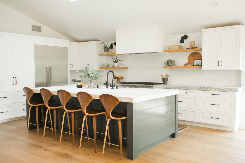 Beach style l-shaped kitchen in Orange County with shaker cabinets, white cabinets, white splashback, subway tile splashback, stainless steel appliances, light hardwood floors, with island, beige floor and grey benchtop.