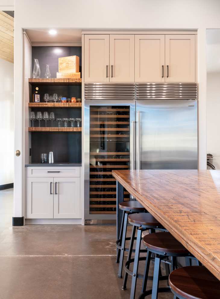 Large country u-shaped open plan kitchen in Denver with a farmhouse sink, shaker cabinets, grey cabinets, wood benchtops, white splashback, marble splashback, stainless steel appliances, concrete floors, with island, brown floor and brown benchtop.