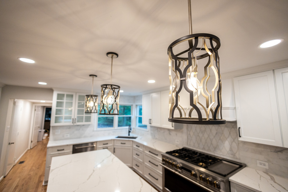 Large transitional l-shaped light wood floor and brown floor eat-in kitchen photo in Baltimore with an undermount sink, shaker cabinets, white cabinets, quartz countertops, white backsplash, marble backsplash, stainless steel appliances, an island and white countertops