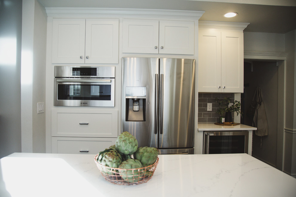 Example of a mid-sized transitional u-shaped porcelain tile enclosed kitchen design in Denver with an undermount sink, shaker cabinets, white cabinets, quartz countertops, beige backsplash, subway tile backsplash, stainless steel appliances and an island