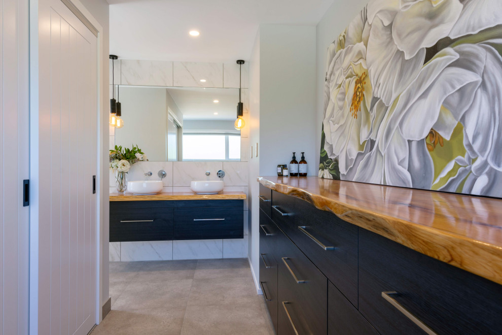 This is an example of a large ensuite bathroom in Wellington with flat-panel cabinets, black cabinets, black and white tiles, marble tiles, white walls, lino flooring, a vessel sink, wooden worktops, grey floors, brown worktops, double sinks and a floating vanity unit.