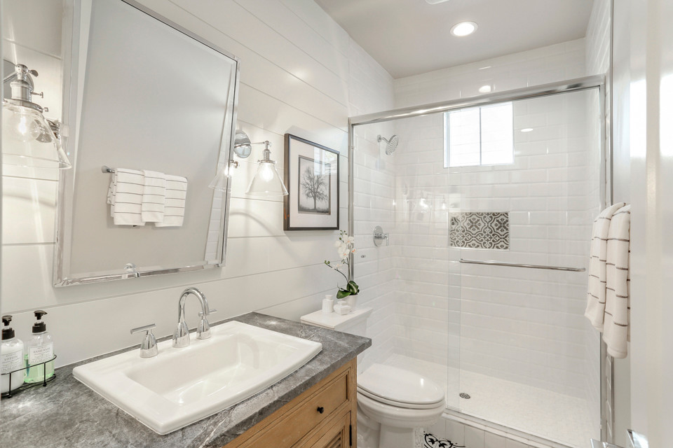 This is an example of a mid-sized country 3/4 bathroom in Sacramento with furniture-like cabinets, grey cabinets, an alcove shower, a two-piece toilet, gray tile, ceramic tile, grey walls, porcelain floors, a drop-in sink, soapstone benchtops, white floor, a sliding shower screen and white benchtops.