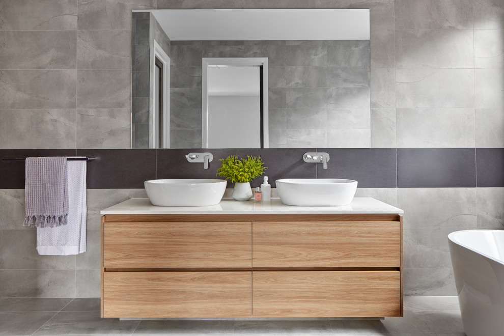 Inspiration for a contemporary master bathroom in Melbourne with flat-panel cabinets, light wood cabinets, a freestanding tub, gray tile, grey walls, a vessel sink, grey floor and white benchtops.