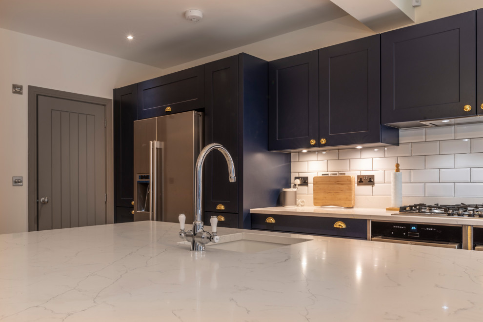 Design ideas for a contemporary eat-in kitchen in Cheshire with shaker cabinets, blue cabinets, white splashback, ceramic splashback, light hardwood floors and with island.