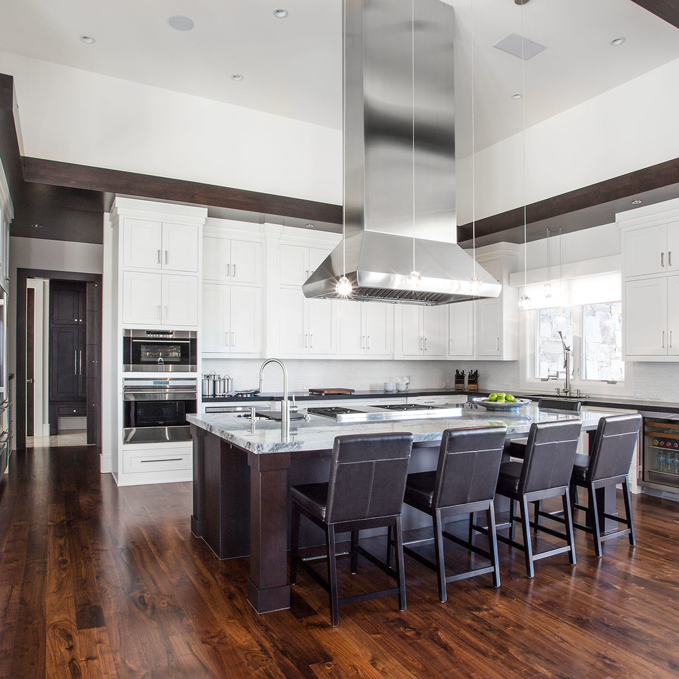 Large contemporary l-shaped eat-in kitchen in Salt Lake City with shaker cabinets, white cabinets, marble benchtops, white splashback, with island, stone tile splashback, stainless steel appliances and dark hardwood floors.