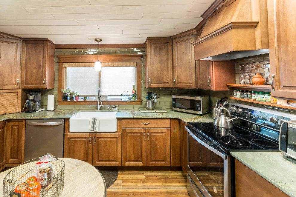 Inredning av ett eklektiskt stort grön grönt kök, med en rustik diskho, luckor med upphöjd panel, bruna skåp, granitbänkskiva, grönt stänkskydd, stänkskydd i glaskakel, rostfria vitvaror, laminatgolv, en halv köksö och brunt golv