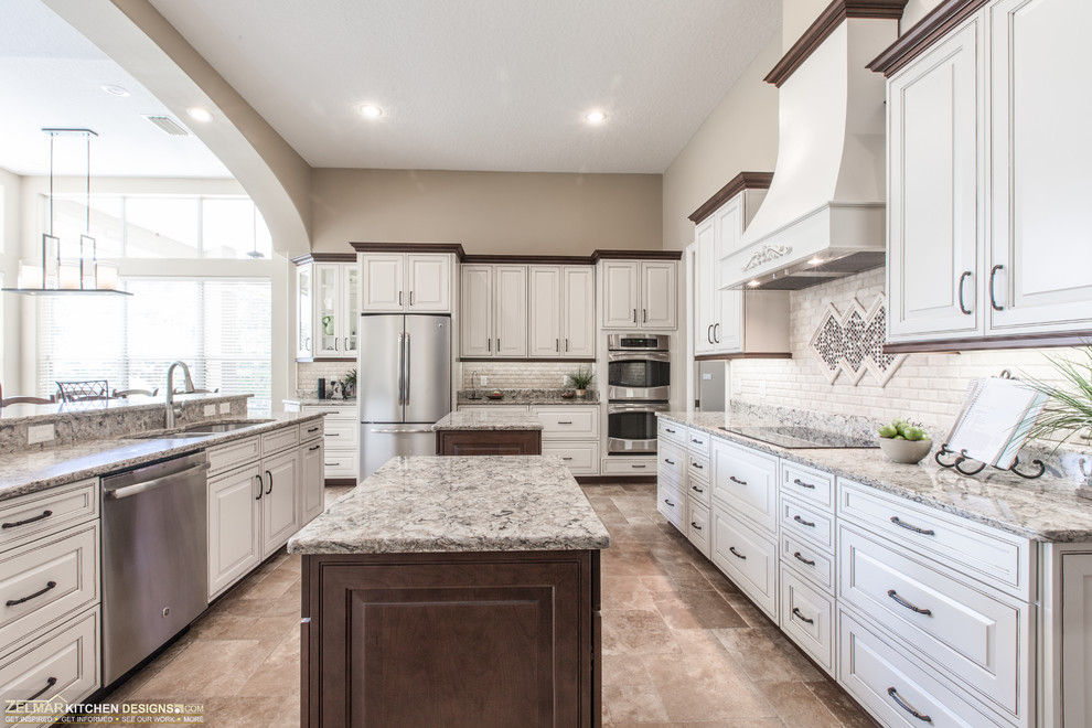 Photo of a large traditional u-shaped eat-in kitchen in Orlando with an undermount sink, raised-panel cabinets, beige cabinets, quartz benchtops, multi-coloured splashback, travertine splashback, stainless steel appliances, travertine floors, multiple islands and multi-coloured floor.