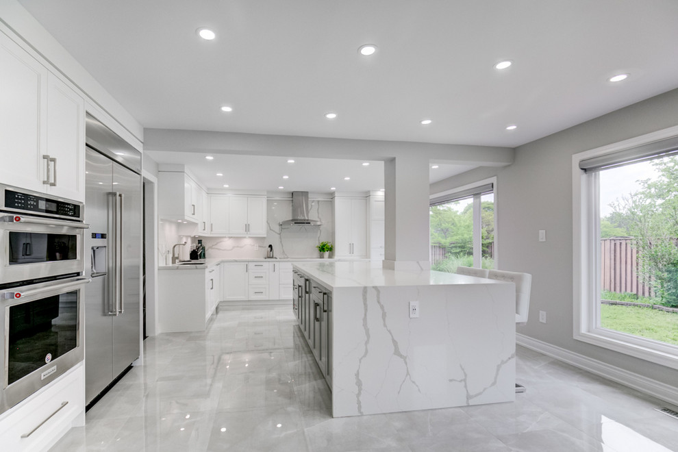 Large contemporary l-shaped eat-in kitchen in Toronto with an undermount sink, shaker cabinets, white cabinets, marble benchtops, white splashback, stone slab splashback, stainless steel appliances, marble floors, with island, grey floor and white benchtop.