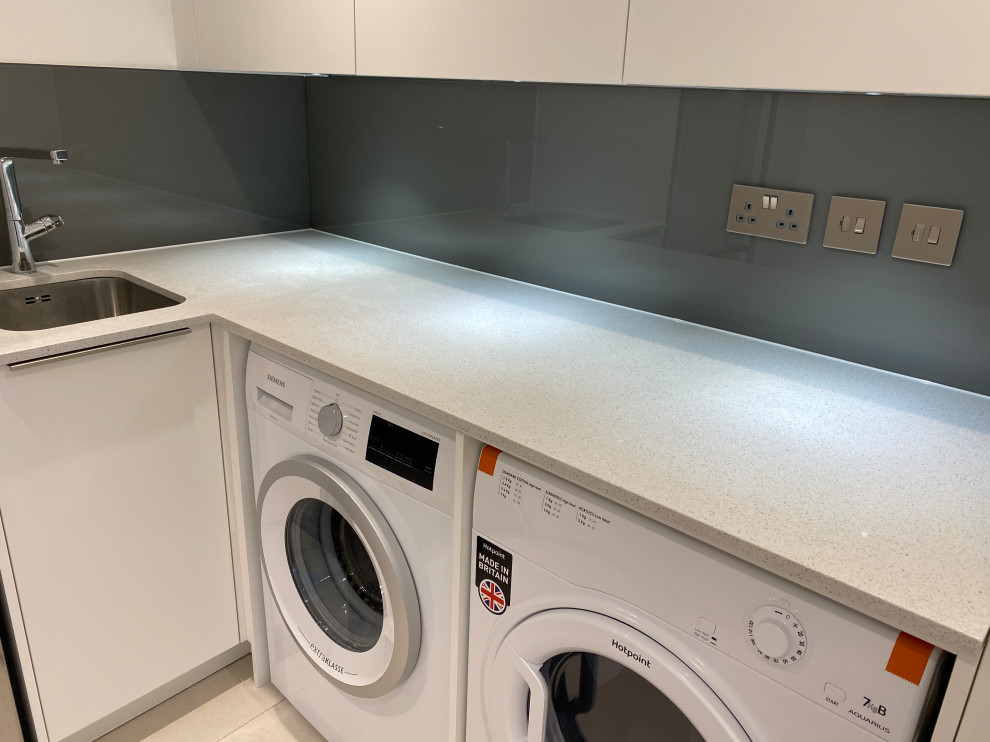 Photo of a small l-shaped utility room in London with flat-panel cabinets, white cabinets, quartzite benchtops, brown splashback, glass sheet splashback, white walls, a side-by-side washer and dryer and white benchtop.