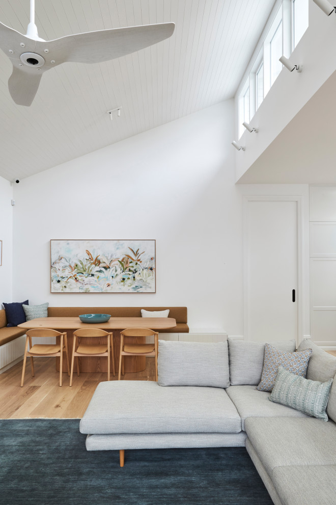 Immagine di una grande sala da pranzo aperta verso il soggiorno con pareti bianche, pavimento in compensato, pavimento marrone e soffitto a volta