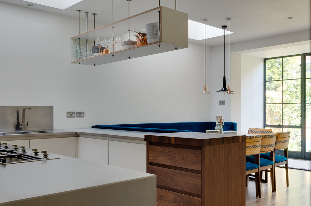 Mid-sized contemporary u-shaped open plan kitchen in London with a drop-in sink, flat-panel cabinets, white cabinets, wood benchtops, metallic splashback, black appliances, light hardwood floors, no island and brown benchtop.