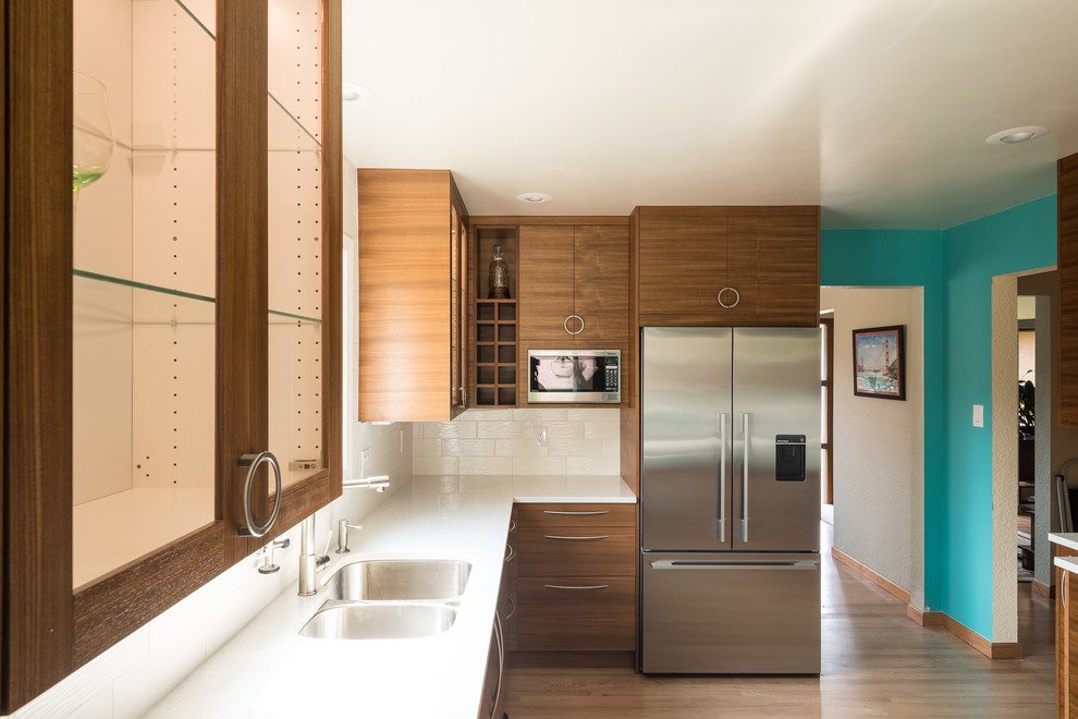 This is an example of a mid-sized midcentury galley kitchen in Seattle with an undermount sink, flat-panel cabinets, medium wood cabinets, quartz benchtops, white splashback, ceramic splashback, stainless steel appliances, light hardwood floors and a peninsula.