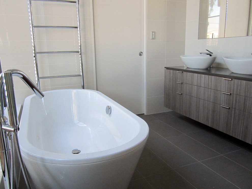 На фото: большая главная ванная комната в стиле модернизм с плоскими фасадами, серыми фасадами, отдельно стоящей ванной, угловым душем, белой плиткой, керамической плиткой, белыми стенами и полом из керамической плитки