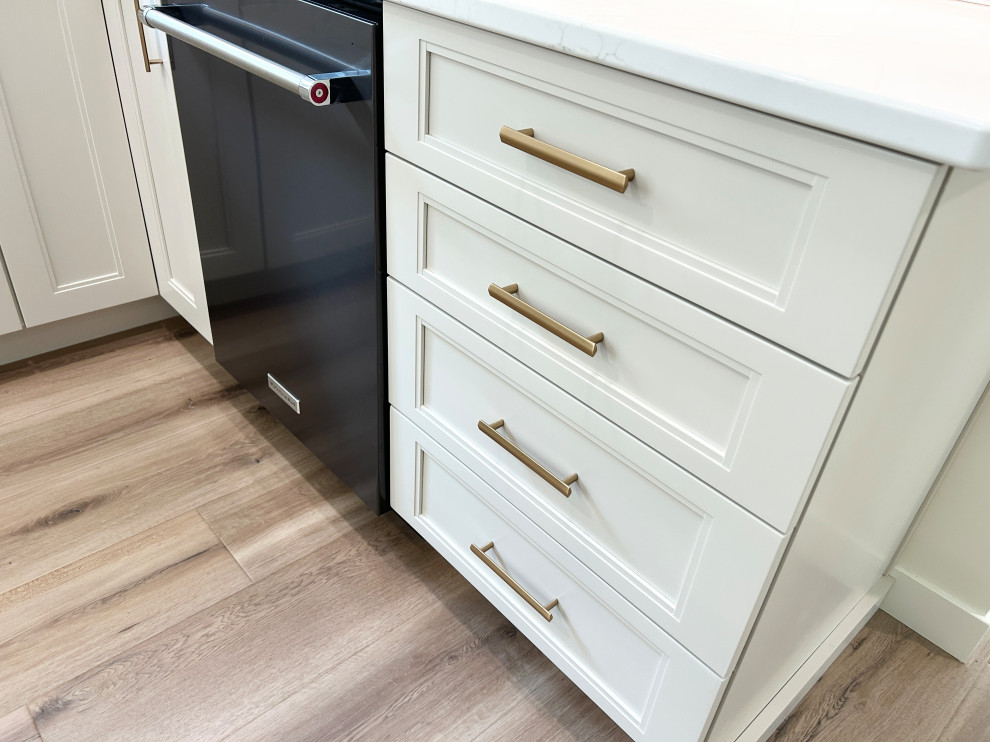 Example of a large transitional u-shaped light wood floor open concept kitchen design with an undermount sink, flat-panel cabinets, white cabinets, quartz countertops, white backsplash, ceramic backsplash, black appliances, an island and white countertops