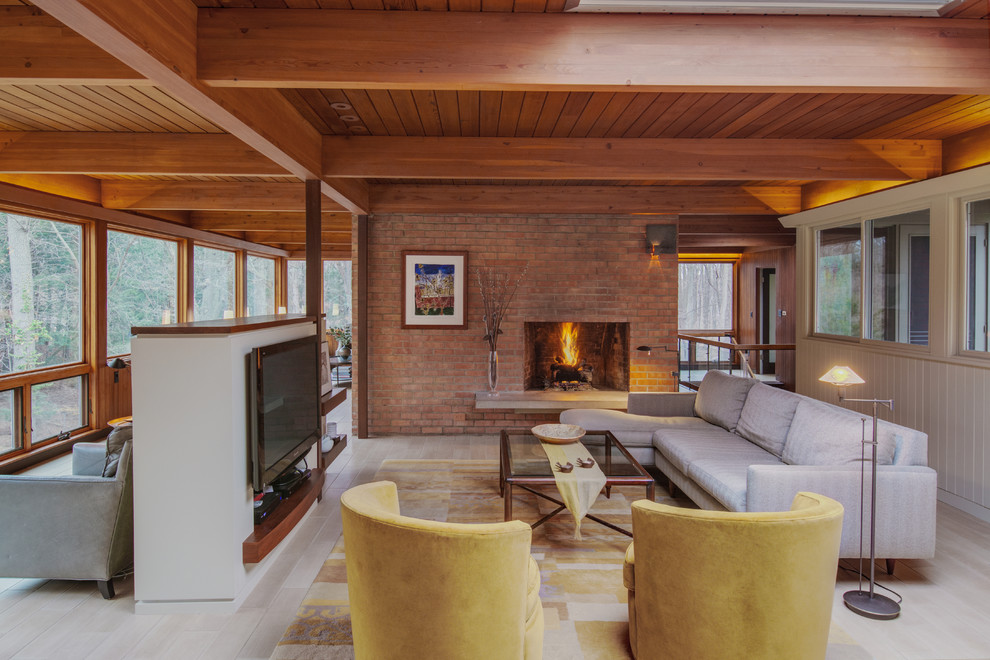 This is an example of a midcentury formal open concept living room in Detroit with a standard fireplace, a brick fireplace surround, a wall-mounted tv and beige floor.