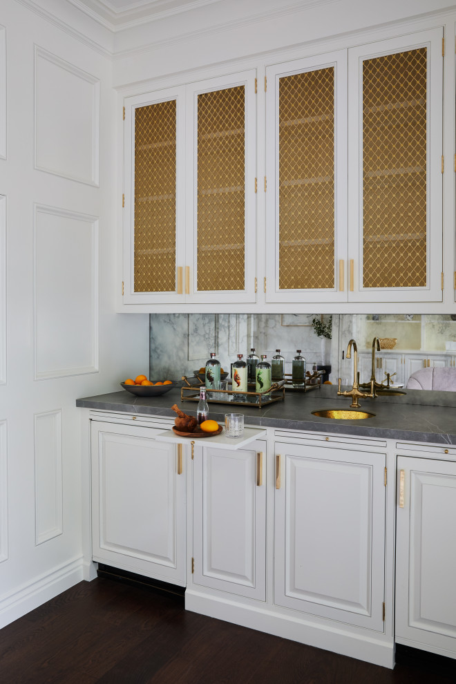 This is an example of a small traditional galley wet bar in Los Angeles with an undermount sink, recessed-panel cabinets, white cabinets, marble benchtops, mirror splashback and grey benchtop.