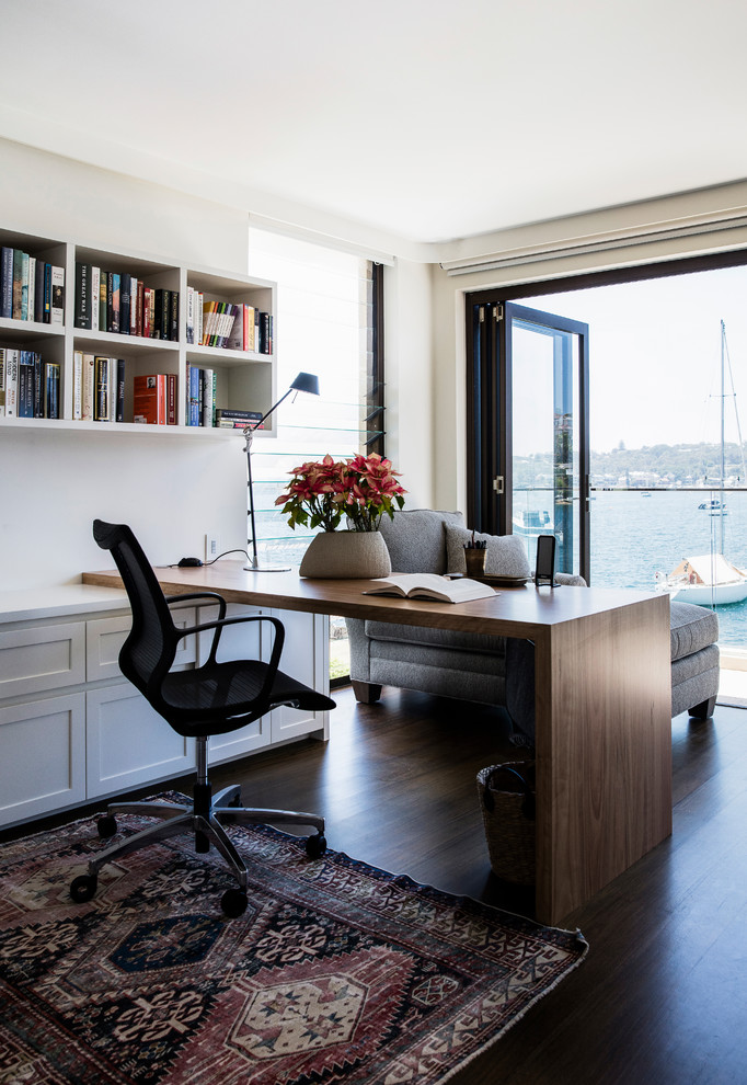 This is an example of a transitional study room in Sydney with beige walls, dark hardwood floors, a built-in desk and brown floor.