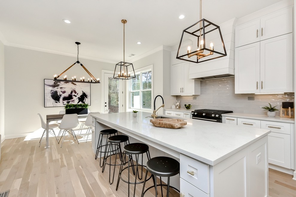 Inspiration for a mid-sized country l-shaped open plan kitchen in Atlanta with an undermount sink, shaker cabinets, white cabinets, quartzite benchtops, grey splashback, ceramic splashback, black appliances, light hardwood floors, with island, beige floor and white benchtop.