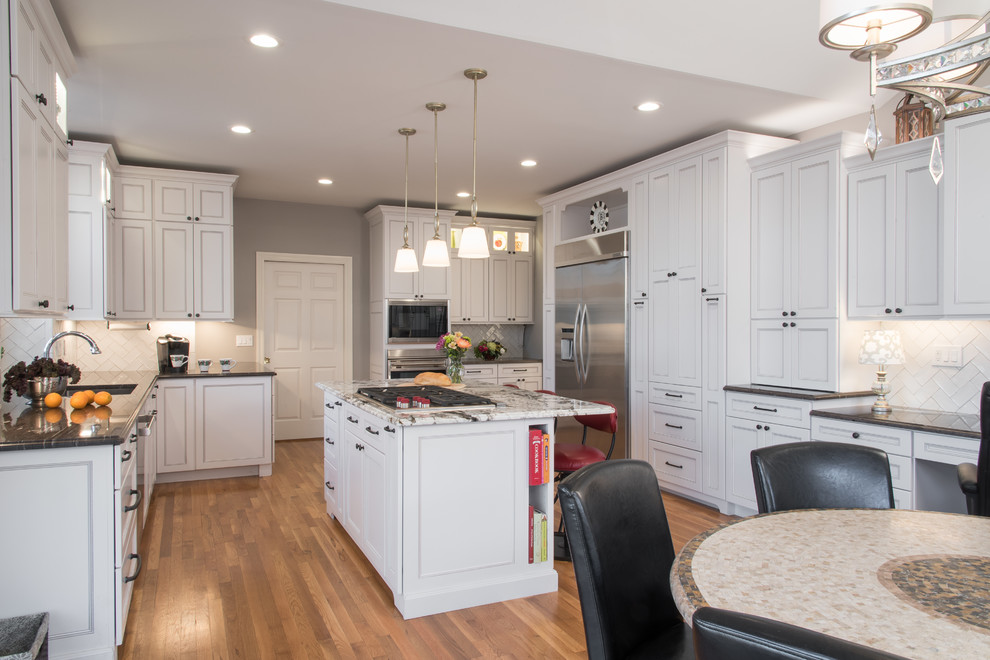 Transitional u-shaped medium tone wood floor enclosed kitchen photo in St Louis with an undermount sink, flat-panel cabinets, white cabinets, granite countertops, white backsplash, subway tile backsplash, stainless steel appliances and an island
