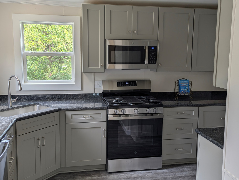 Example of a small transitional l-shaped gray floor enclosed kitchen design with a single-bowl sink, flat-panel cabinets, gray cabinets, granite countertops, stainless steel appliances and black countertops