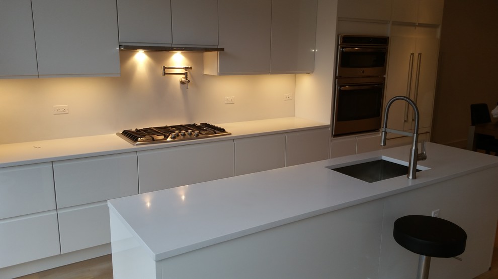 Large modern u-shaped eat-in kitchen in New York with flat-panel cabinets, white cabinets, with island, a drop-in sink, marble benchtops, white splashback, stainless steel appliances, light hardwood floors and brown floor.