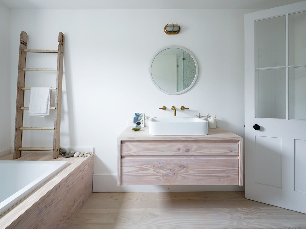 Inspiration for a mid-sized scandinavian master bathroom in Other with light wood cabinets, an alcove shower, white walls, light hardwood floors, a vessel sink, wood benchtops, a drop-in tub and beige benchtops.