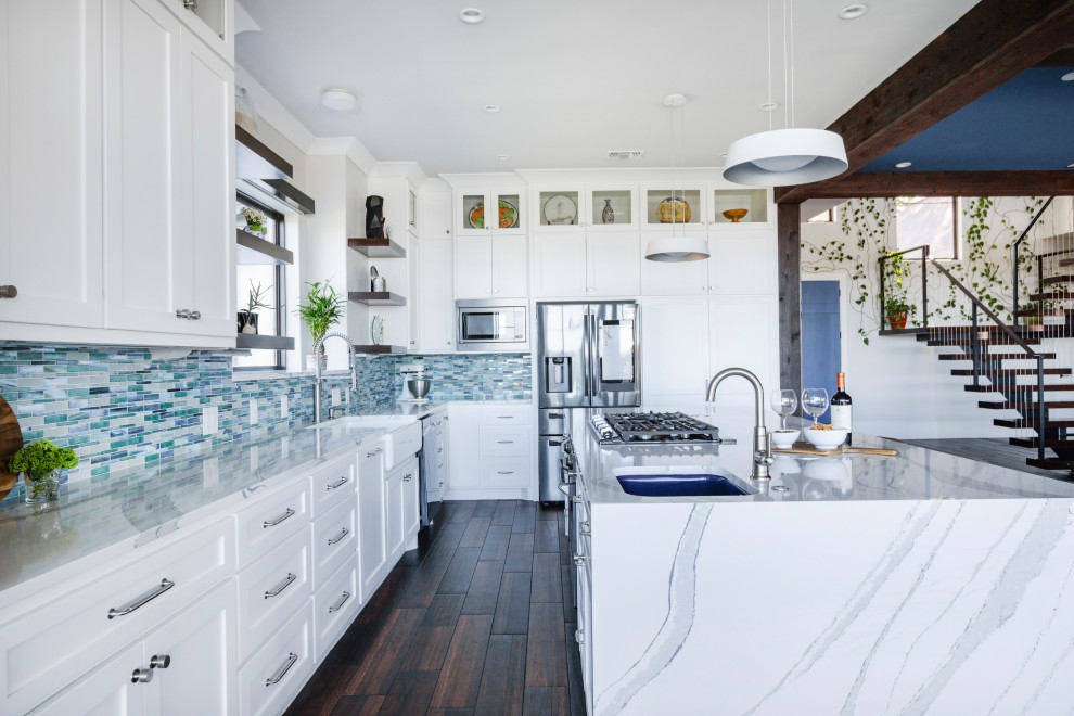 Inspiration for a mid-sized contemporary l-shaped open plan kitchen in Houston with a farmhouse sink, raised-panel cabinets, white cabinets, quartzite benchtops, blue splashback, glass tile splashback, stainless steel appliances, dark hardwood floors, with island, brown floor, white benchtop and exposed beam.