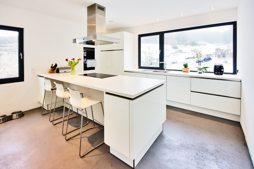 This is an example of a large contemporary single-wall open plan kitchen in Frankfurt with glass-front cabinets, white cabinets, solid surface benchtops, with island, concrete floors and a drop-in sink.