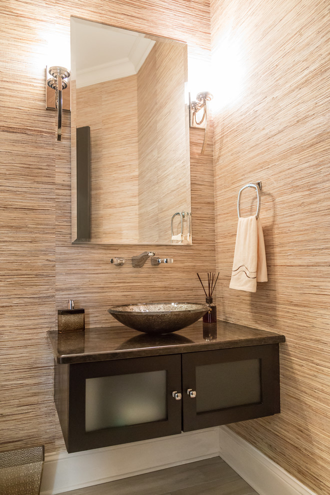 This is an example of a large contemporary bathroom with glass-front cabinets, dark wood cabinets, a two-piece toilet, brown walls, ceramic floors, a vessel sink, granite benchtops, grey floor and brown benchtops.
