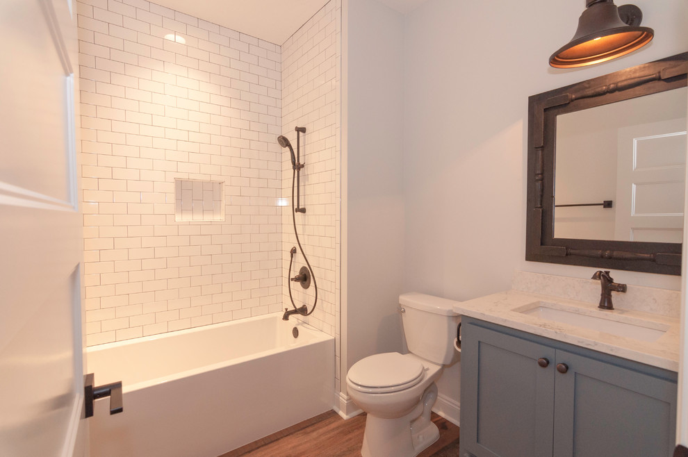 Design ideas for a large arts and crafts kids bathroom in Other with shaker cabinets, blue cabinets, an alcove tub, a shower/bathtub combo, a two-piece toilet, white tile, subway tile, white walls, vinyl floors, an undermount sink, engineered quartz benchtops, brown floor, a shower curtain and white benchtops.