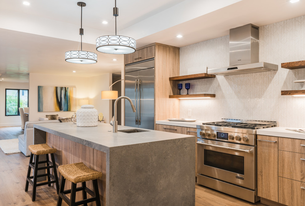 Photo of a contemporary galley kitchen in Santa Barbara with an undermount sink, flat-panel cabinets, brown cabinets, white splashback, mosaic tile splashback, stainless steel appliances, medium hardwood floors, with island and brown floor.