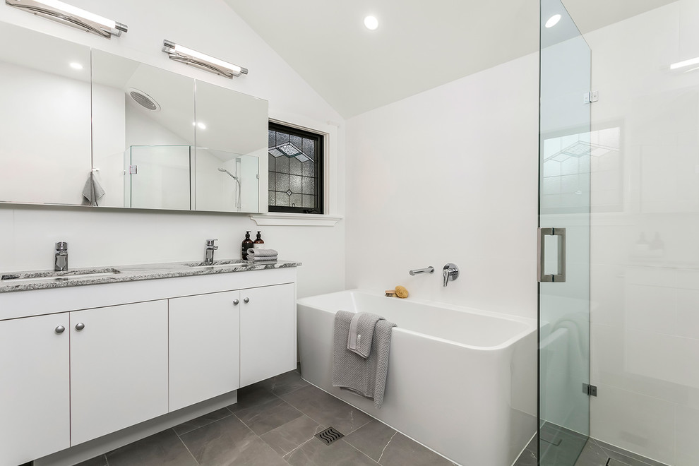 Design ideas for a contemporary master bathroom in Melbourne with white walls, grey floor, a hinged shower door, flat-panel cabinets, white cabinets, a drop-in tub, a corner shower, an undermount sink and grey benchtops.