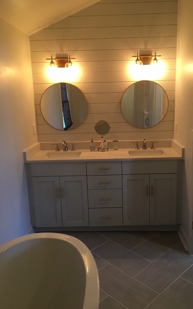 This is an example of a mid-sized transitional master bathroom in Charlotte with recessed-panel cabinets, white cabinets, a freestanding tub, an alcove shower, a two-piece toilet, white walls, ceramic floors, an integrated sink, grey floor, quartzite benchtops, white benchtops, gray tile, ceramic tile and a hinged shower door.