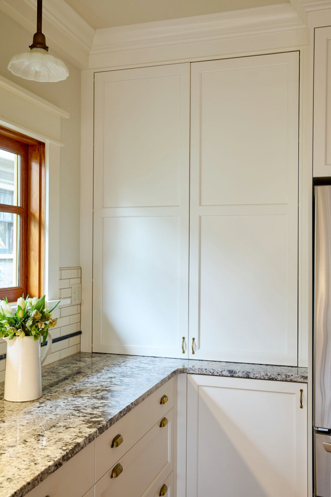 Photo of a mid-sized transitional kitchen pantry in Portland with an undermount sink, recessed-panel cabinets, white cabinets, granite benchtops, white splashback, ceramic splashback, stainless steel appliances, medium hardwood floors, with island, brown floor and multi-coloured benchtop.