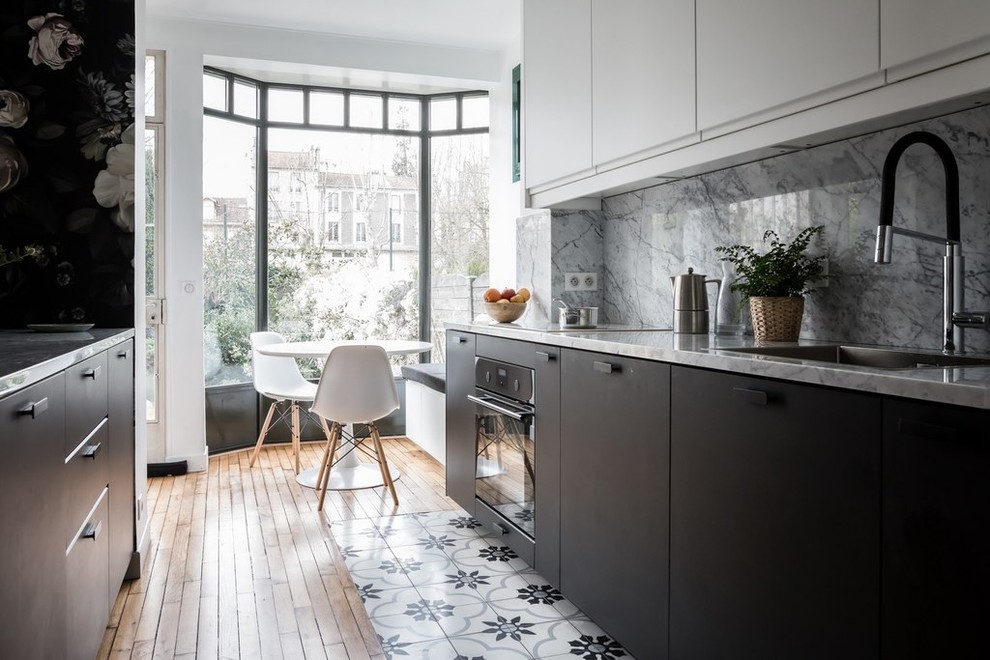 Inspiration for a mid-sized contemporary galley eat-in kitchen in Paris with an undermount sink, flat-panel cabinets, black cabinets, marble benchtops, grey splashback, marble splashback, black appliances, cement tiles, with island, multi-coloured floor and grey benchtop.