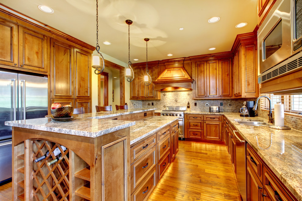 Large mountain style u-shaped light wood floor and brown floor eat-in kitchen photo with a double-bowl sink, raised-panel cabinets, medium tone wood cabinets, an island, granite countertops, multicolored backsplash, stone tile backsplash and stainless steel appliances