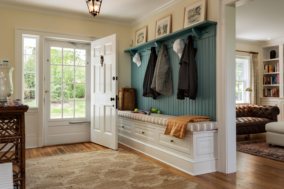This is an example of a large traditional mudroom in New York with yellow walls, a single front door and a white front door.